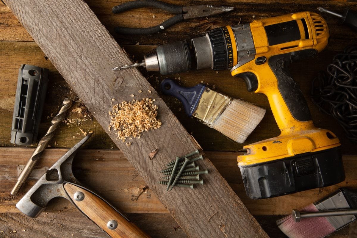 Cordless drill and hand tools on a wooden workbench