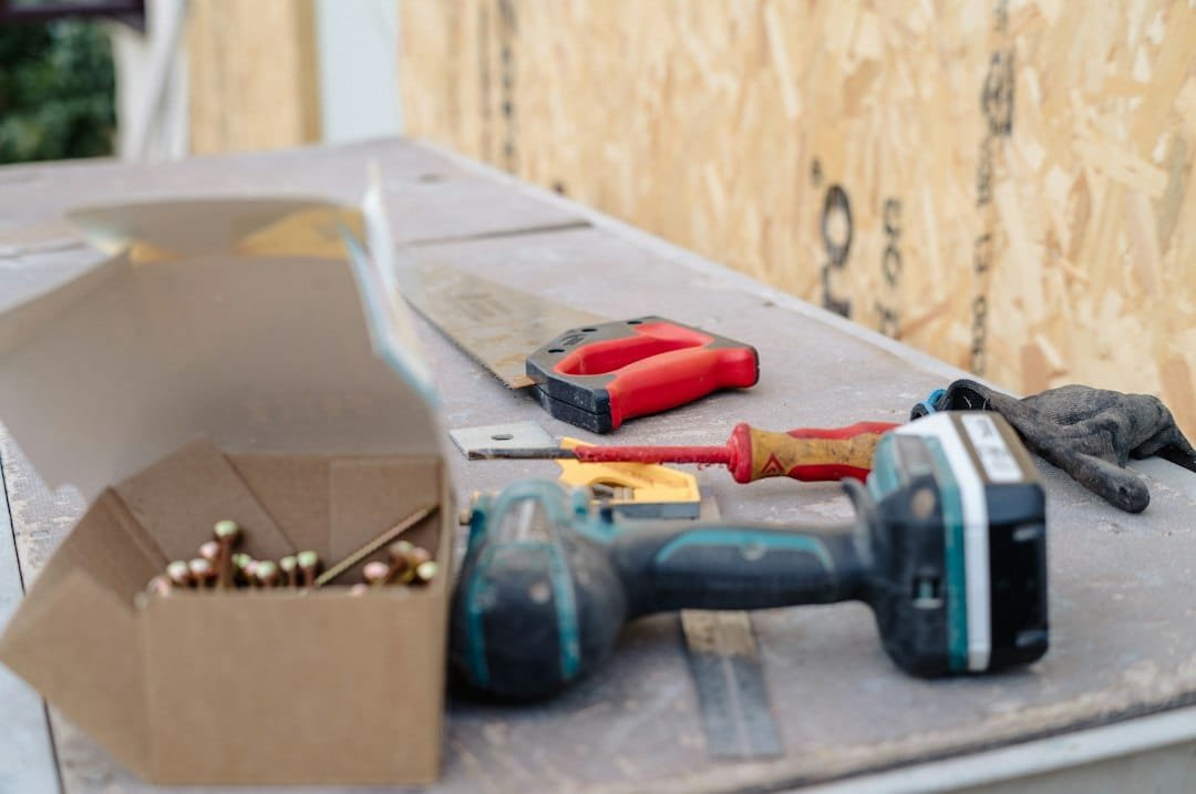 Power drill, screwdriver, and construction tools on wooden surface